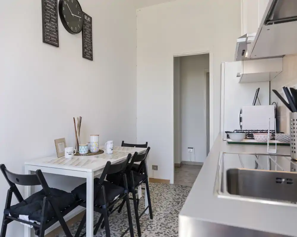 Cuisine compacte et lumineuse avec une petite table pour quatre et un évier/stove en acier inoxydable sur la droite. Décor simple et soigné, adapté aux locations courte durée.