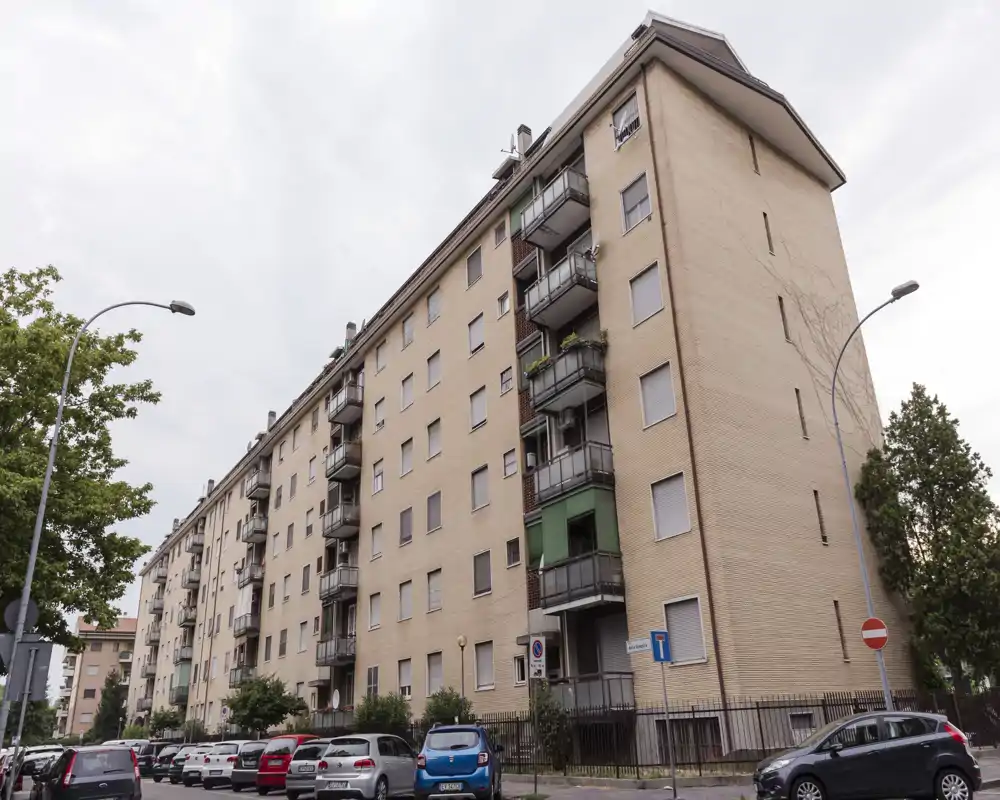 Vue extérieure d'un immeuble résidentiel de plusieurs étages avec balcons donnant sur une rue bordée de voitures — adapté pour présenter la façade et le quartier.