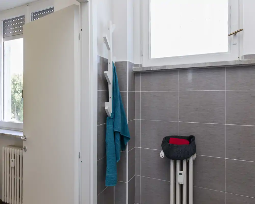 Coin de salle de bain avec murs carrelés, radiateur et patères ; lumière naturelle par une fenêtre haute et finitions modernes et soignées.