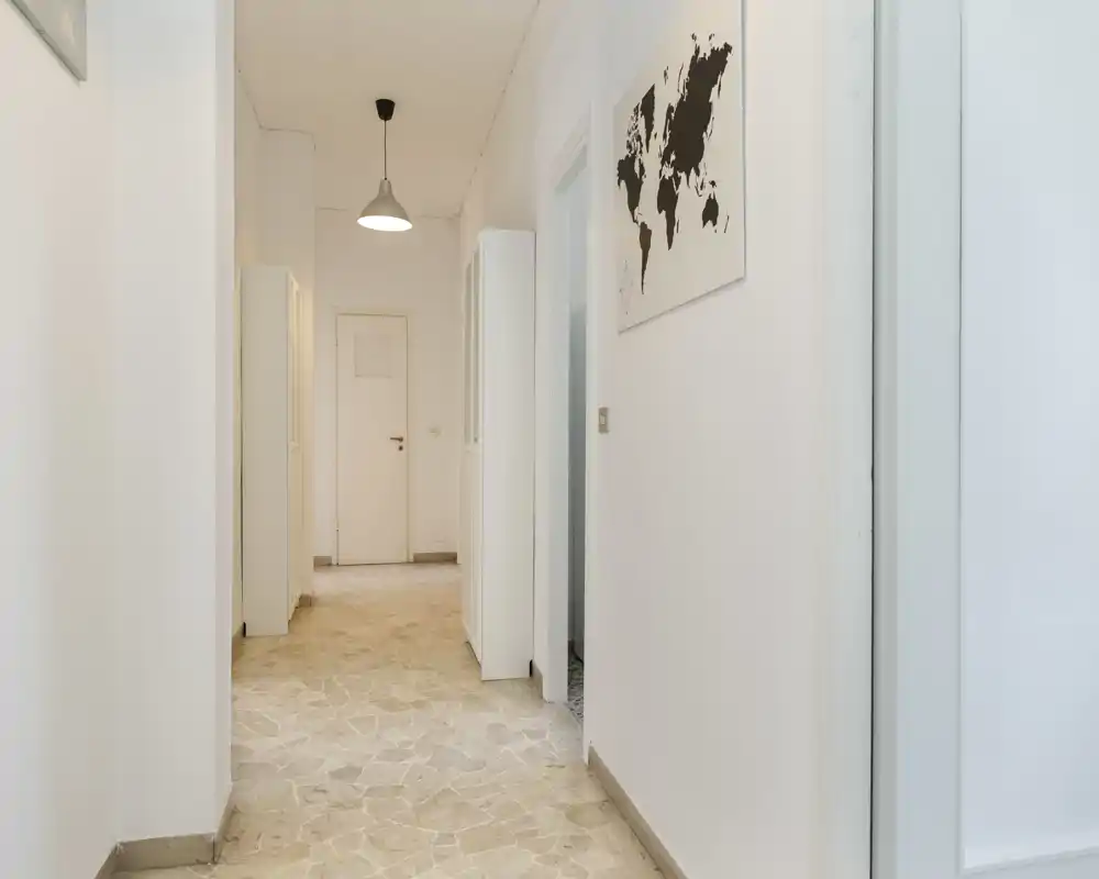 Entrée/couloir lumineux et minimaliste avec murs neutres, suspension et sol en carrelage pierre — un espace de transition propre menant aux pièces intérieures.