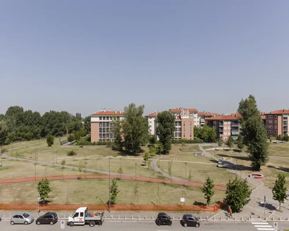 Grande espace vert commun avec sentiers et arbres matures devant des immeubles résidentiels bas, pris en plein jour — idéal pour mettre en valeur les équipements extérieurs.