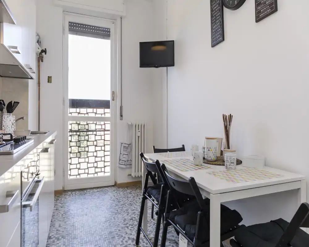 Cuisine compacte et lumineuse avec une table pour quatre, électroménagers modernes et lumière naturelle depuis la porte du balcon — parfaite pour un séjour citadin.