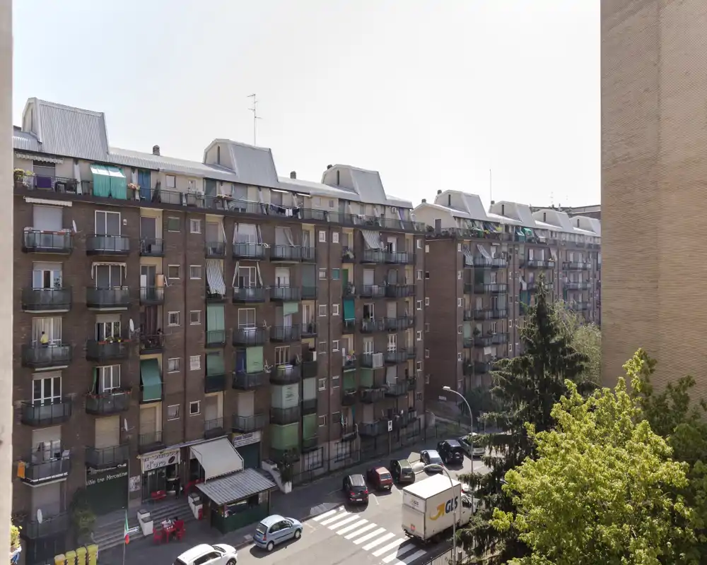 Vue extérieure sur la rue montrant un immeuble avec plusieurs balcons, voitures garées et arbres — utile pour présenter l’emplacement et la façade du bâtiment.