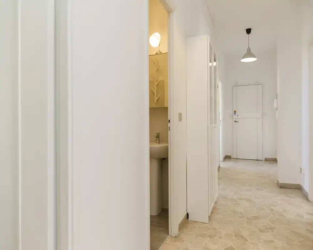 Entrée lumineuse et minimaliste avec sol en carrelage, murs blancs et suspension lumineuse — espace d'accueil propre et accueillant.