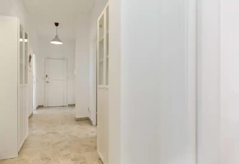Ingresso luminoso e pulito con pavimento in pietra, pareti bianche e un lampadario a sospensione centrale — ottima prima impressione per un affitto.