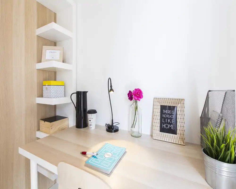 Espacio de trabajo en casa, luminoso y ordenado, con escritorio de madera, jarrón con flores, marco decorativo y estantes — ideal para leer o teletrabajar.