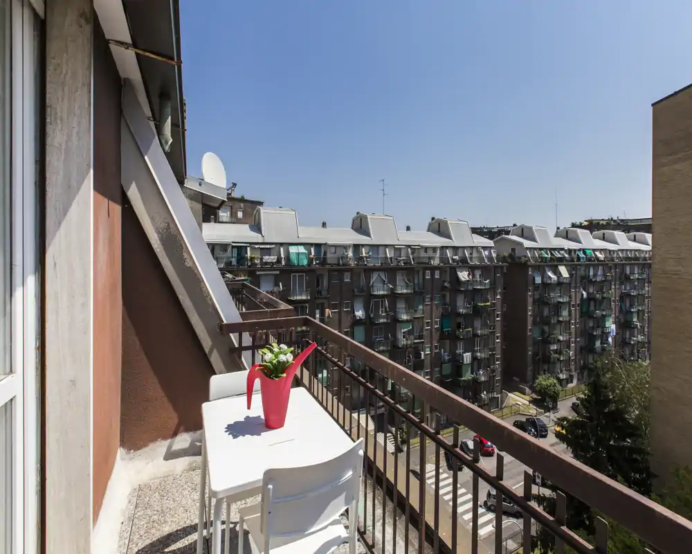 Balcón soleado con una pequeña mesa blanca y sillas, con vistas a un bloque residencial — ideal para el café de la mañana con vistas urbanas.
