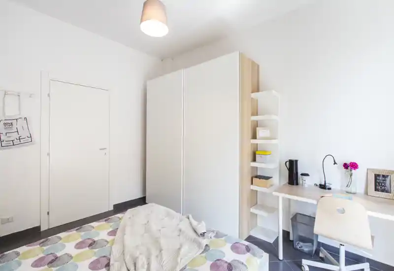 Camera singola luminosa e moderna con copriletto colorato, grande armadio bianco e scrivania compatta: ideale per studenti o soggiorni brevi.