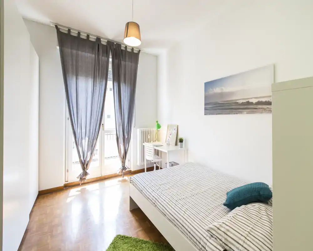 Dormitorio luminoso y bien decorado con cama doble, almohadones y un pequeño escritorio junto a la ventana que aporta mucha luz natural.