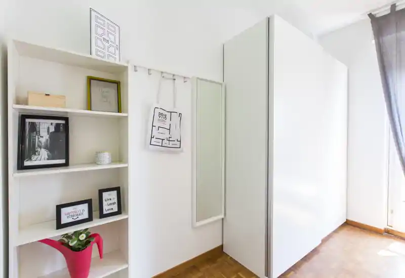 Entrée lumineuse avec une grande armoire blanche, un miroir mural et des étagères décorées de cadres et d'une plante. Lumière naturelle venant de la droite.