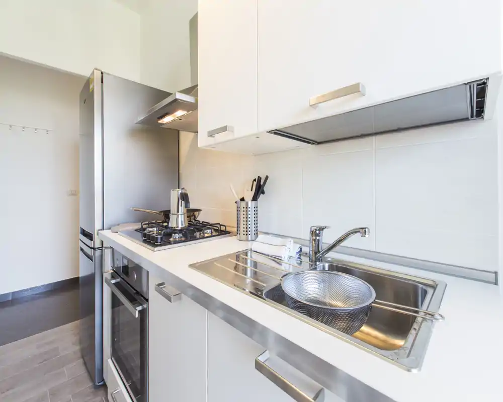 Cocina moderna y compacta con electrodomésticos de acero inoxidable, placa de gas, horno y fregadero doble. Superficies limpias y luminosas con utensilios prácticos, lista para cocinar a diario.