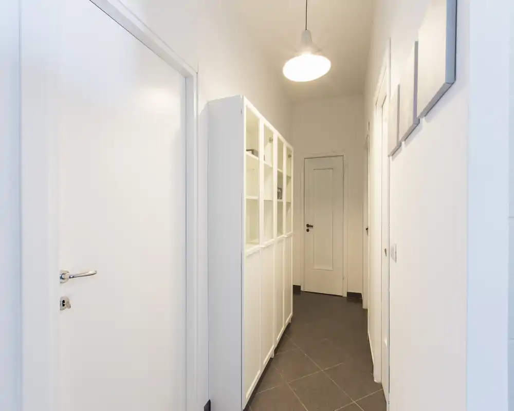 Entrada/pasillo estrecho y luminoso con paredes blancas, un armario alto y una lámpara colgante: diseño limpio y minimalista ideal para un piso.