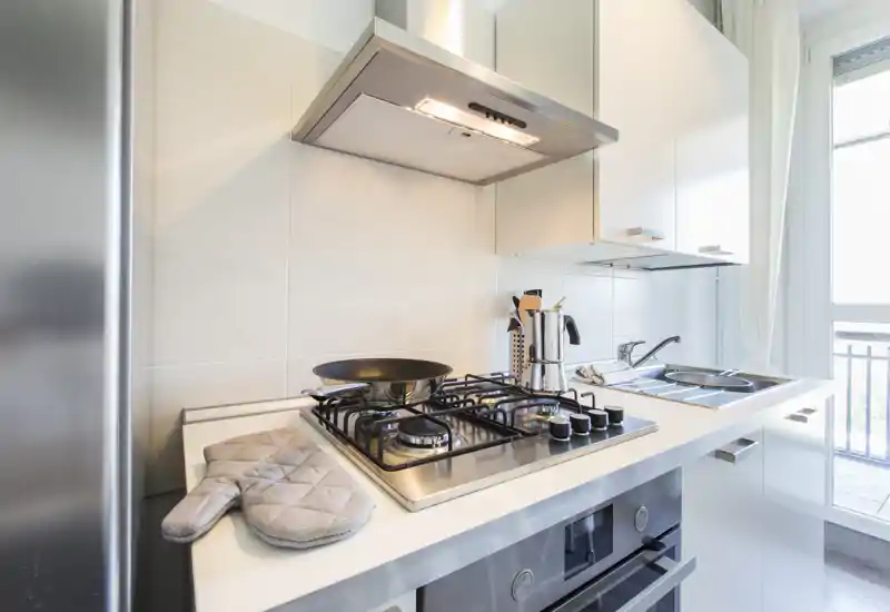 Coin cuisine moderne et lumineux avec plaque à gaz, hotte, évier en inox et accessoires soignés sur le plan de travail, comme un manique et des ustensiles.