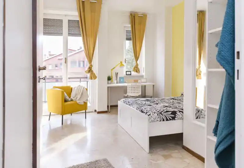 Dormitorio luminoso y estiloso con cama blanca estampada, butaca amarilla acogedora y un escritorio junto a la ventana — mucha luz natural y acentos en amarillo.