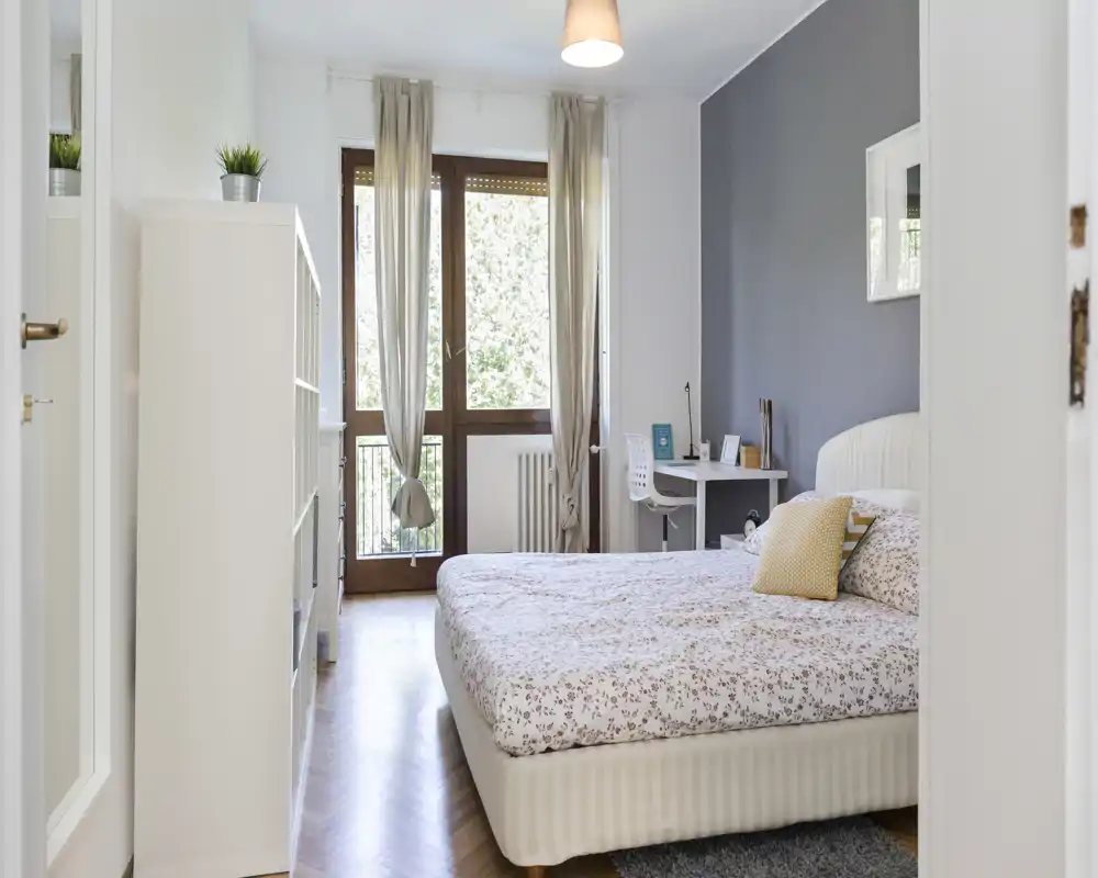 Bright, well-styled bedroom with a comfortable double bed, soft linens and a desk near the window offering natural light and a pleasant view.