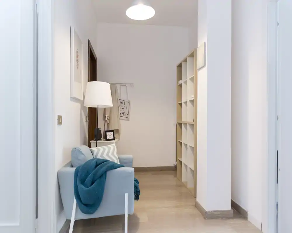 Well-lit entrance/hallway with a small armchair, floor lamp and shelving — ideal as a welcoming foyer or reading nook.