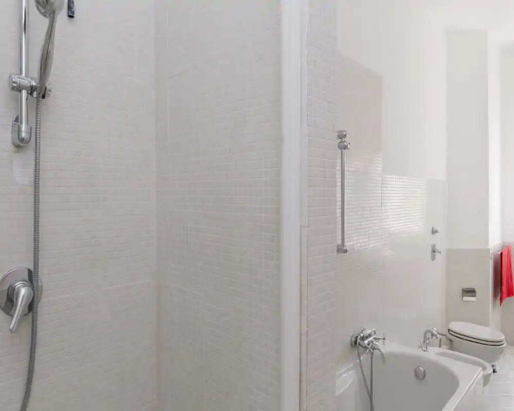 Bright, modern bathroom with a walk-in shower head, bathtub and toilet; light mosaic tiles and clean, minimal design.