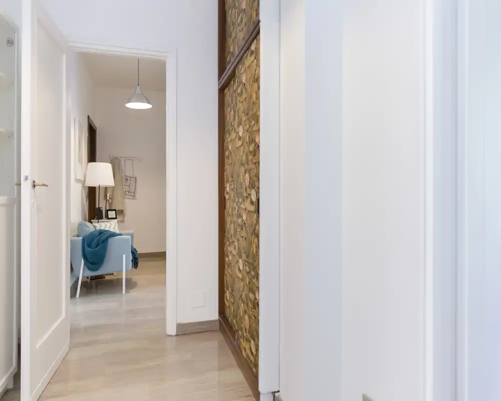Bright, clean entrance/hallway with light marble floor and a glimpse into a living area featuring a pale blue armchair and floor lamp.