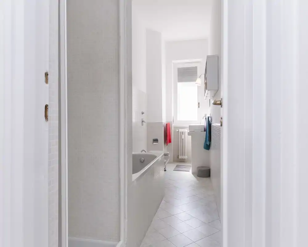 Bright, clean bathroom with bathtub, sink and window; neutral tiles and natural light create a fresh, minimal look.