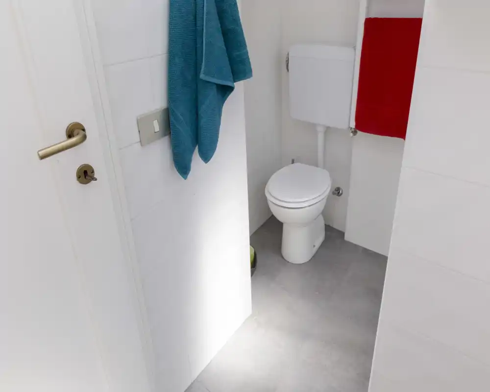 Compact, clean bathroom with a toilet, tiled walls and floor, and colorful towels providing contrast.