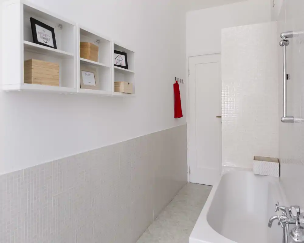 Bright, minimal bathroom with a built-in bathtub, tiled walls and open shelving; clean white finishes and a small towel hook add practical touches.