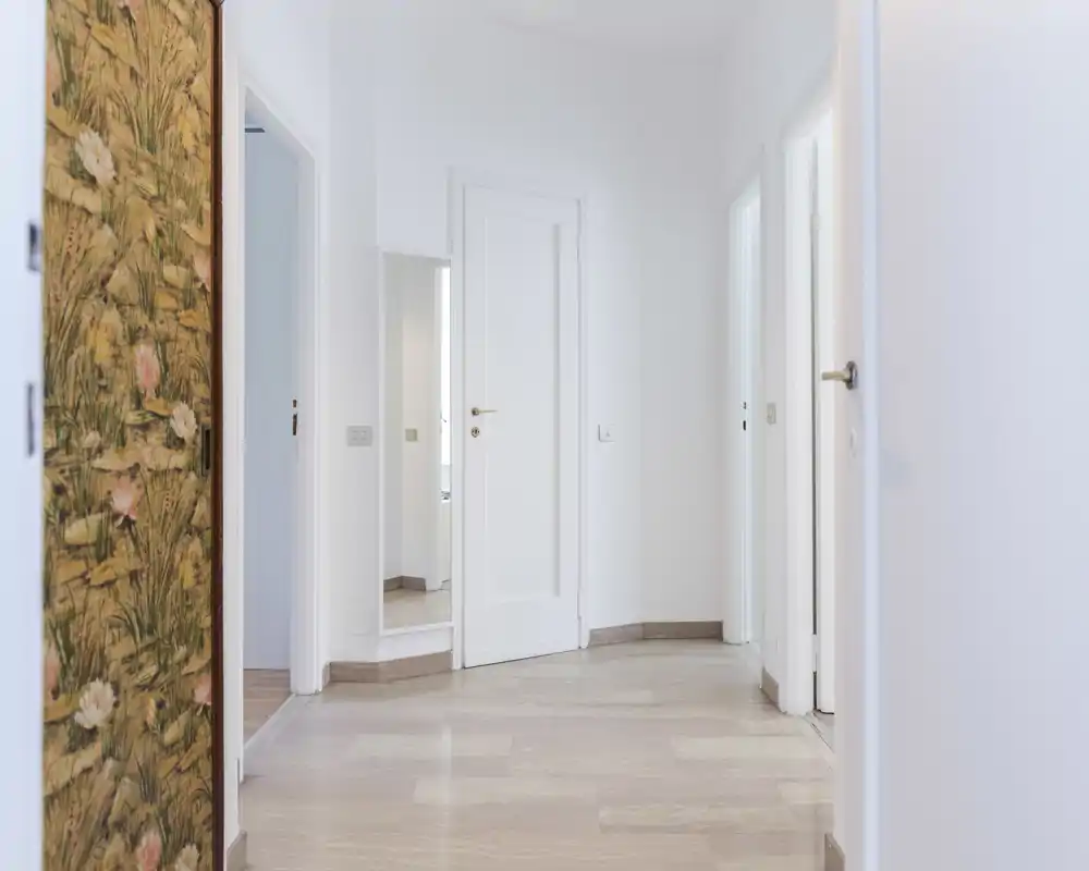 Bright, minimalist entrance/hallway with white walls, light wooden floor and multiple doorways creating a clean, airy first impression.