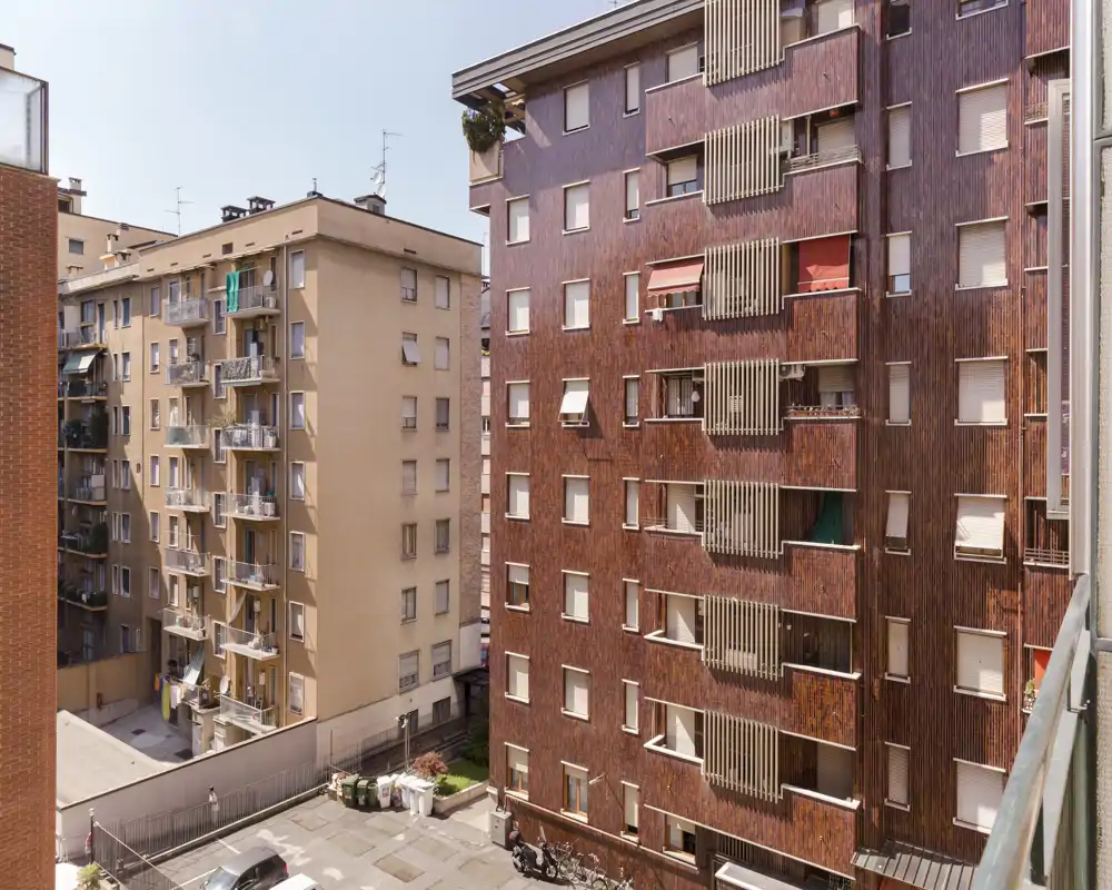 View from a balcony/window onto neighboring apartment buildings and a small courtyard; clear daylight photo showing façade details and street-level elements.