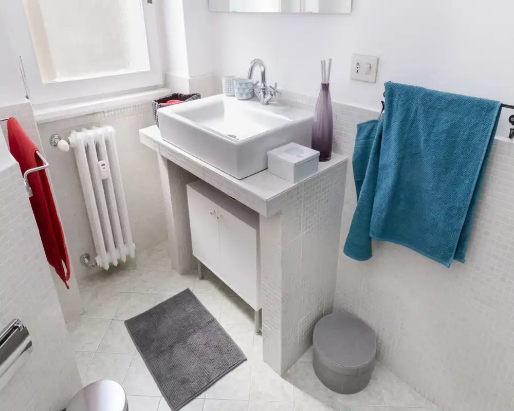Bright, clean bathroom with a modern countertop sink, towel rails and tiled surfaces. Natural light from a frosted window enhances the fresh, tidy appearance.