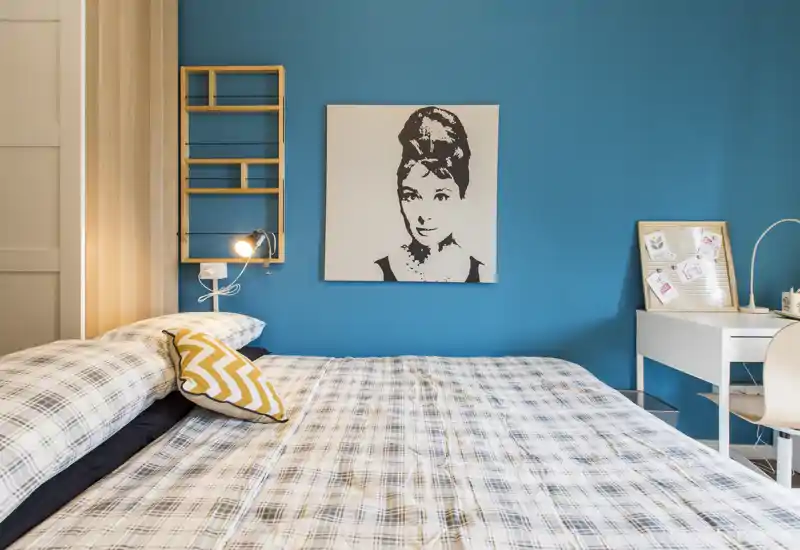 Dormitorio luminoso y con estilo con cama grande, ropa de cama estampada y pared azul turquesa con cuadro, además de un pequeño escritorio: acogedor y bien presentado para alquileres.