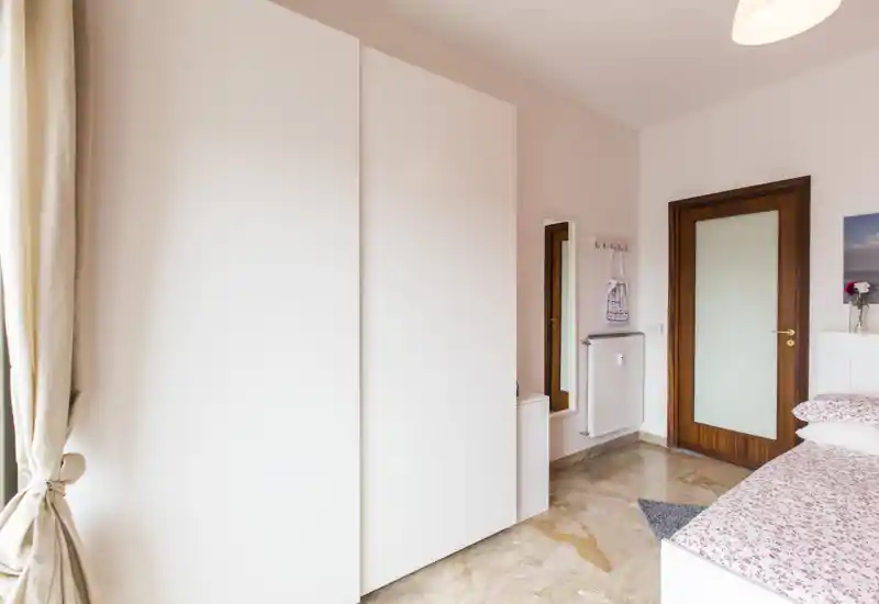 Dormitorio luminoso y ordenado con armario blanco, ropa de cama estampada y luz natural desde la ventana; perfecto para fotos de alquiler que buscan transmitir limpieza y serenidad.