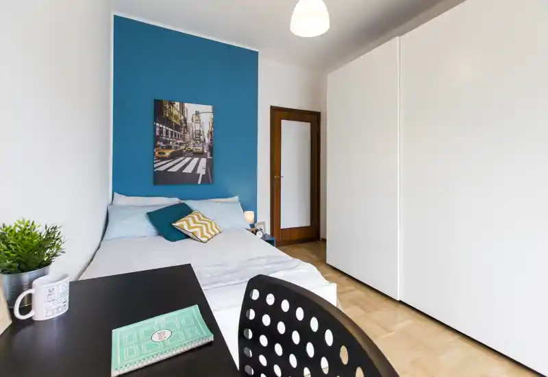 Dormitorio luminoso y moderno con pared de acento turquesa, cama cómoda, escritorio en primer plano y un gran armario blanco — ideal para estudiantes o profesionales.