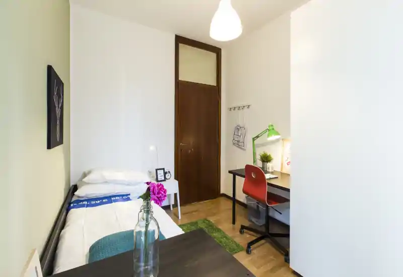 Dormitorio individual compacto y bien decorado con cama, mesita y escritorio. Ambiente luminoso y acogedor, perfecto para estudiante o huésped individual.