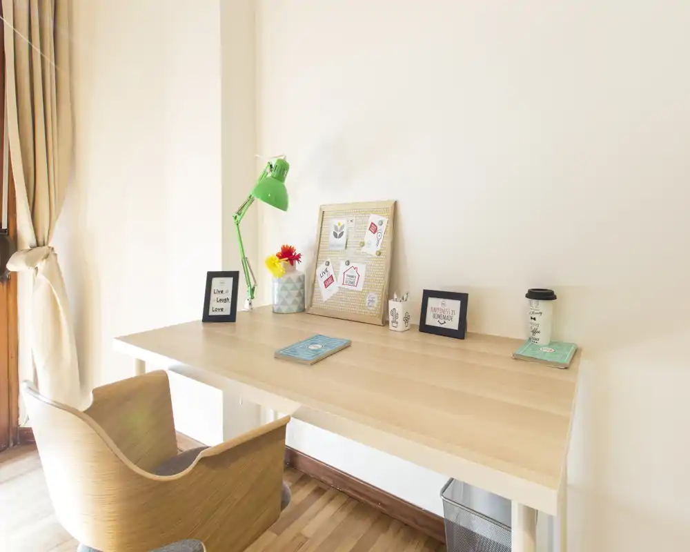 Espacio de trabajo luminoso y minimalista con escritorio y silla de madera, lámpara verde y pequeños detalles decorativos — superficie ordenada ideal para estudiar o trabajar.