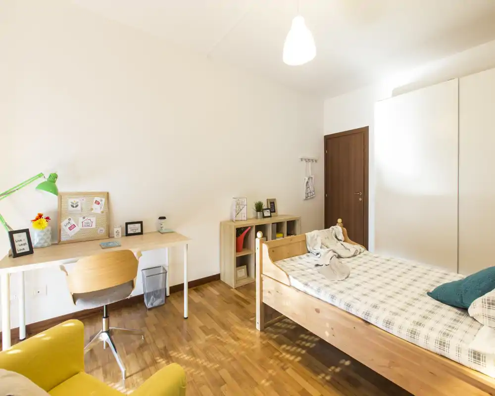 Dormitorio individual luminoso y bien decorado con cama de madera, escritorio y armario — ideal para una estancia cómoda. Suelo de parquet cálido y buena iluminación.