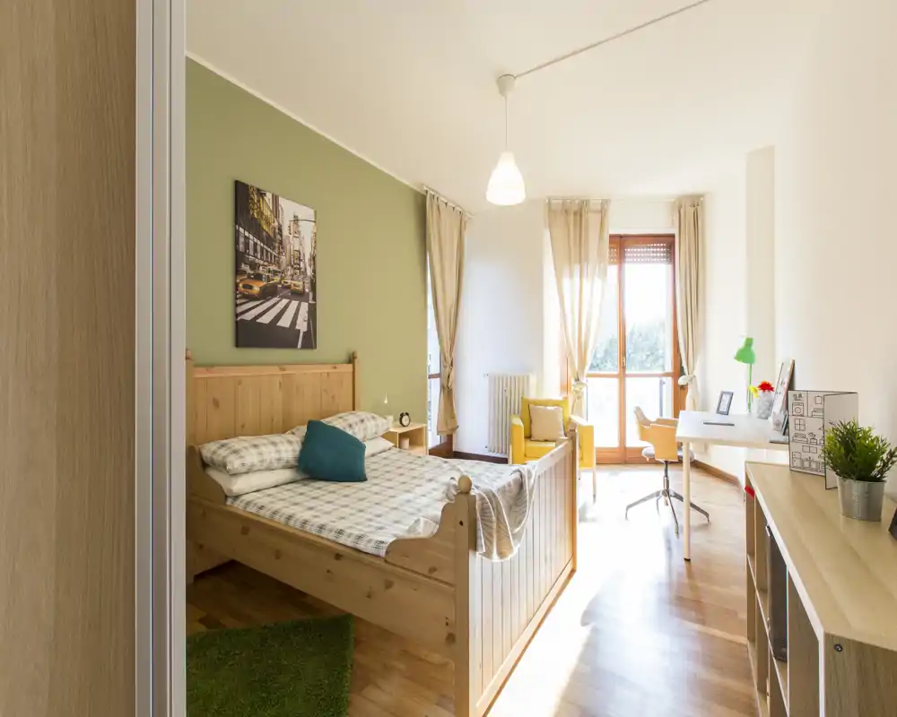 Dormitorio luminoso y bien decorado con cama doble de madera, ropa de cama acogedora, cojín y zona de trabajo junto a la ventana.