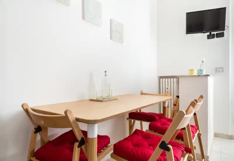 Coin repas compact avec table en bois clair et quatre chaises pliantes garnies de coussins rouges ; cadre lumineux et minimaliste idéal pour des repas décontractés.