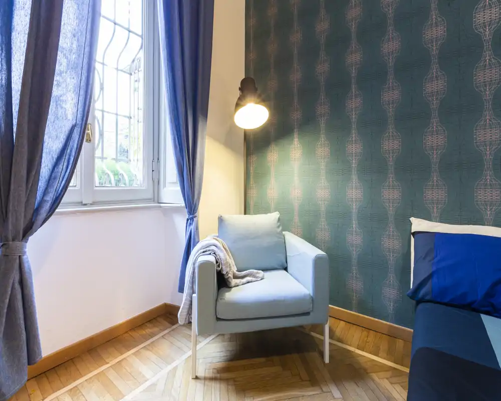 Bright, stylish seating corner with a comfortable armchair, soft throw and decorative wallpaper next to a window — ideal for relaxing or reading.