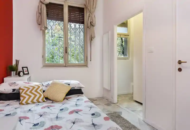 Dormitorio luminoso y acogedor con colcha estampada, cojines decorativos y una gran ventana que aporta luz natural.