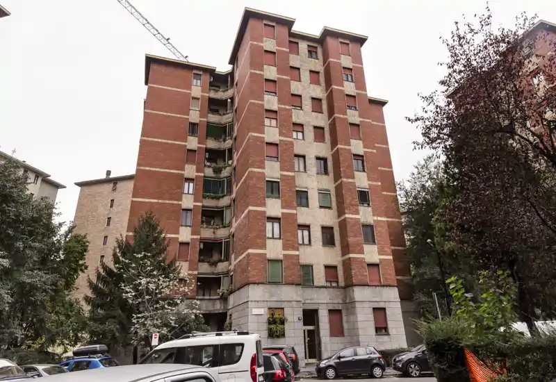 Exterior view of a multi-story residential building with parked cars and trees in front — this photo shows the building facade and surroundings, not an interior room.