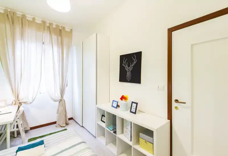 Camera da letto luminosa e ordinata con letto a righe, contenitori a cubo e finestra con tende svolazzanti; arredo moderno e luminoso.