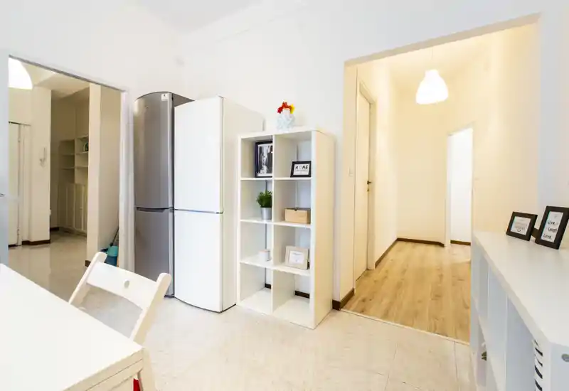 Bright, modern kitchen corner with fridge, open shelving and simple dining furniture — clean lines and decorative accents create a welcoming space.