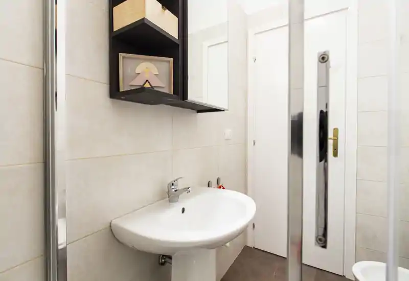 Small, modern bathroom with a white pedestal sink, tiled walls and a mirrored shower door; clean and well lit.