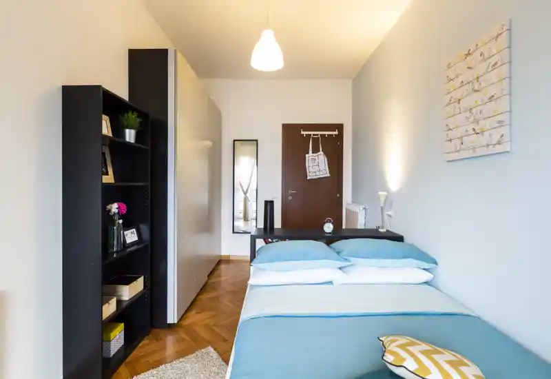 Dormitorio individual moderno y luminoso con ropa de cama turquesa, suelo de parquet y almacenamiento ordenado; ideal para alquileres de corta estancia o estudiantes.