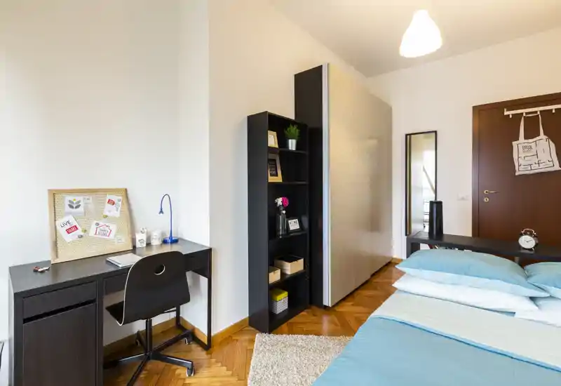 Dormitorio moderno y luminoso con cama bien hecha, mesita y un escritorio junto a una estantería — ideal para trabajar y descansar.