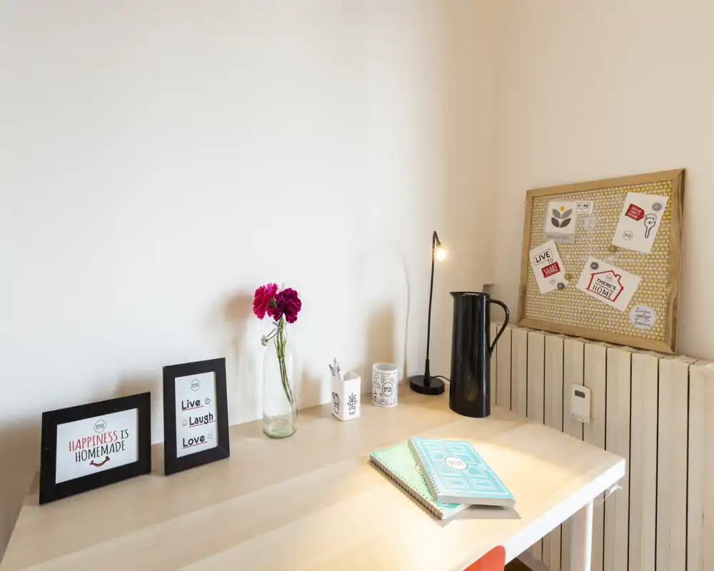 Angolo luminoso e curato con stampe incorniciate, vaso di fiori e lampada — uno spazio accogliente per lavorare o leggere.