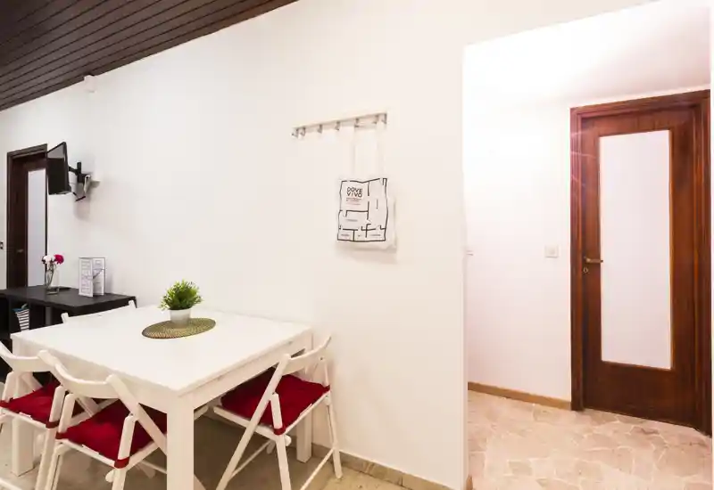 Bright, modern dining area with a white table, four chairs with red cushions and simple decorative accents—ideal for small meals or a cozy work spot.