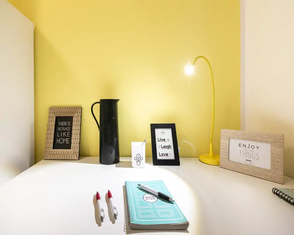 Bright, styled desk nook with decorative frames, a yellow task lamp and tidy stationery — ideal for working or reading in a cozy corner.