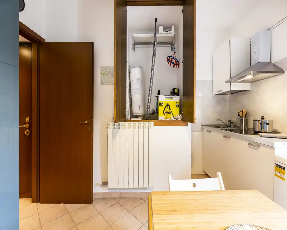 Compact, tidy kitchen with white cabinets, extractor hood and a small dining table in the foreground; practical storage and appliances are visible.