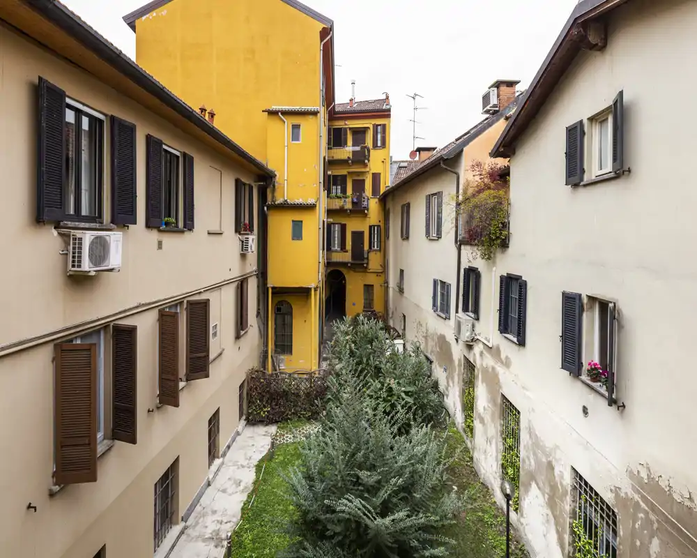 Quiet inner courtyard view with neighboring apartment facades, shutters and a small planted area — ideal to show building context and exterior common space.