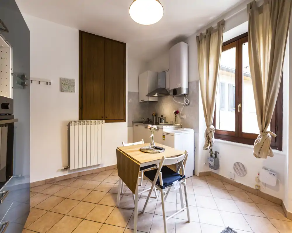 Compact, well-lit kitchen with a small dining table, modern hood and large window letting in natural light — cozy and functional for a small apartment.